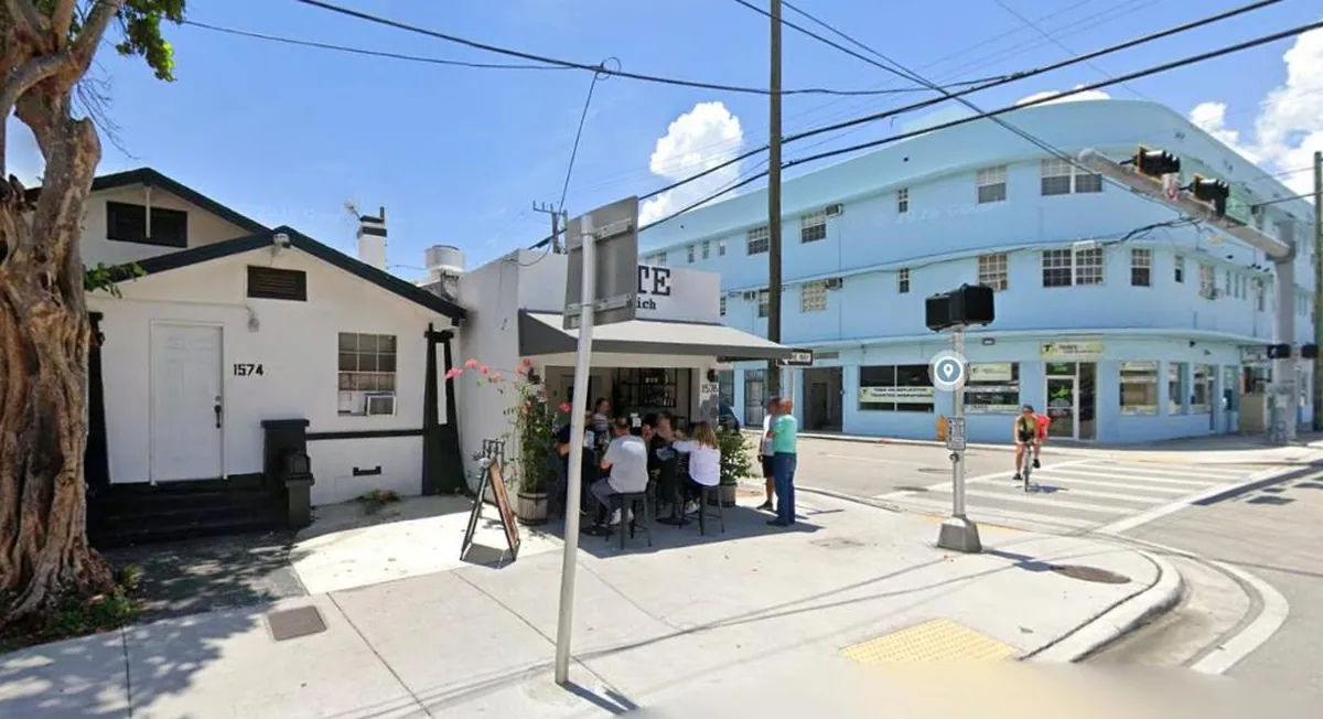 BITE Sandwich's white corner building on SW 1st Street, with customers on stools under a small awning