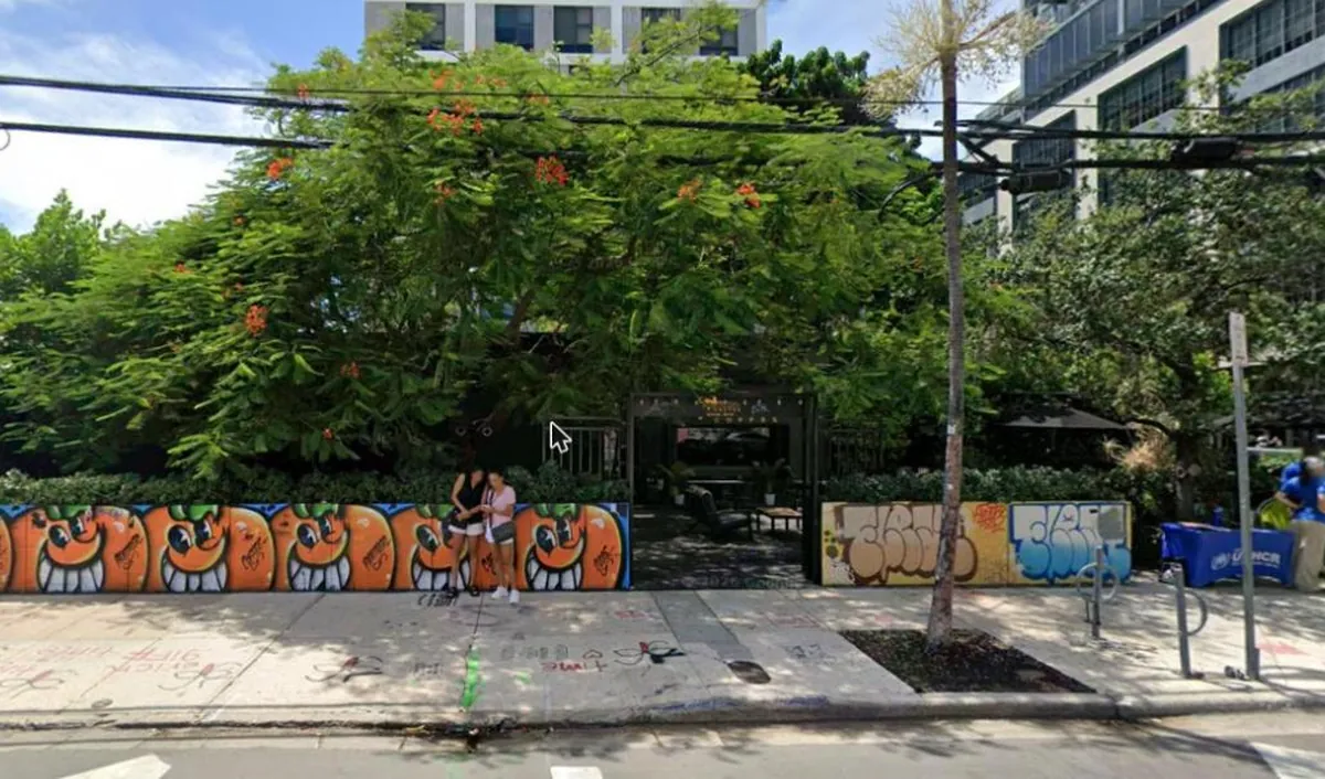 Panther Coffee's garden entrance on NW 2nd Avenue in Wynwood, behind a low mural wall and a flowering tree